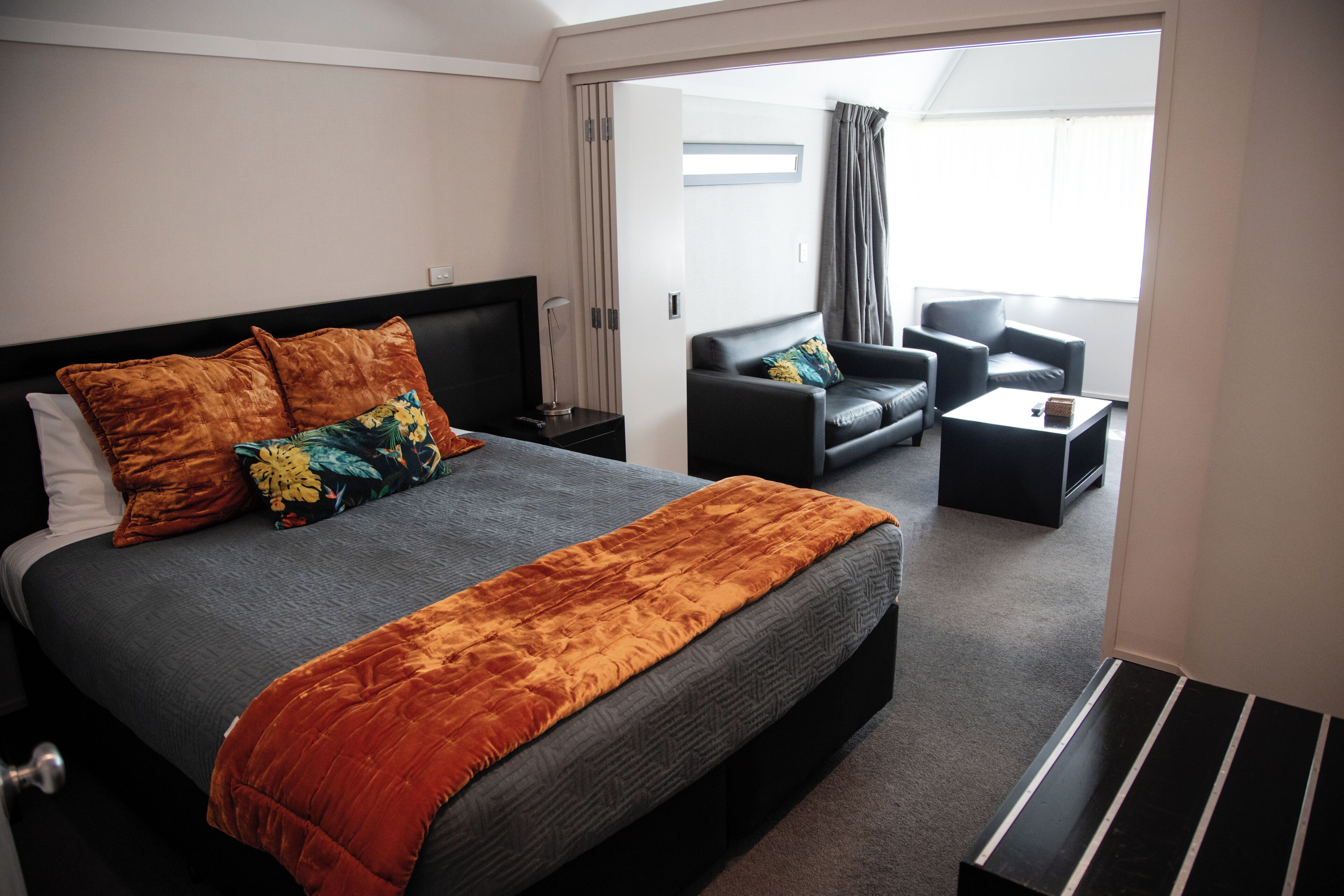 A hotel room with a large bed, a sofa, a coffee table, and a view of the outside.