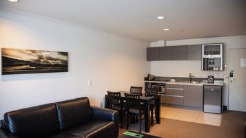 Un apartamento moderno con sala de estar que incluye un sofá de cuero negro, una mesa de comedor con sillas, una cocina con armarios grises y un refrigerador.