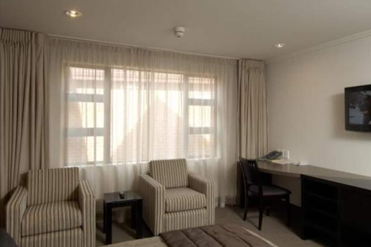 A hotel room with a bed, two armchairs, a desk, and a chair.