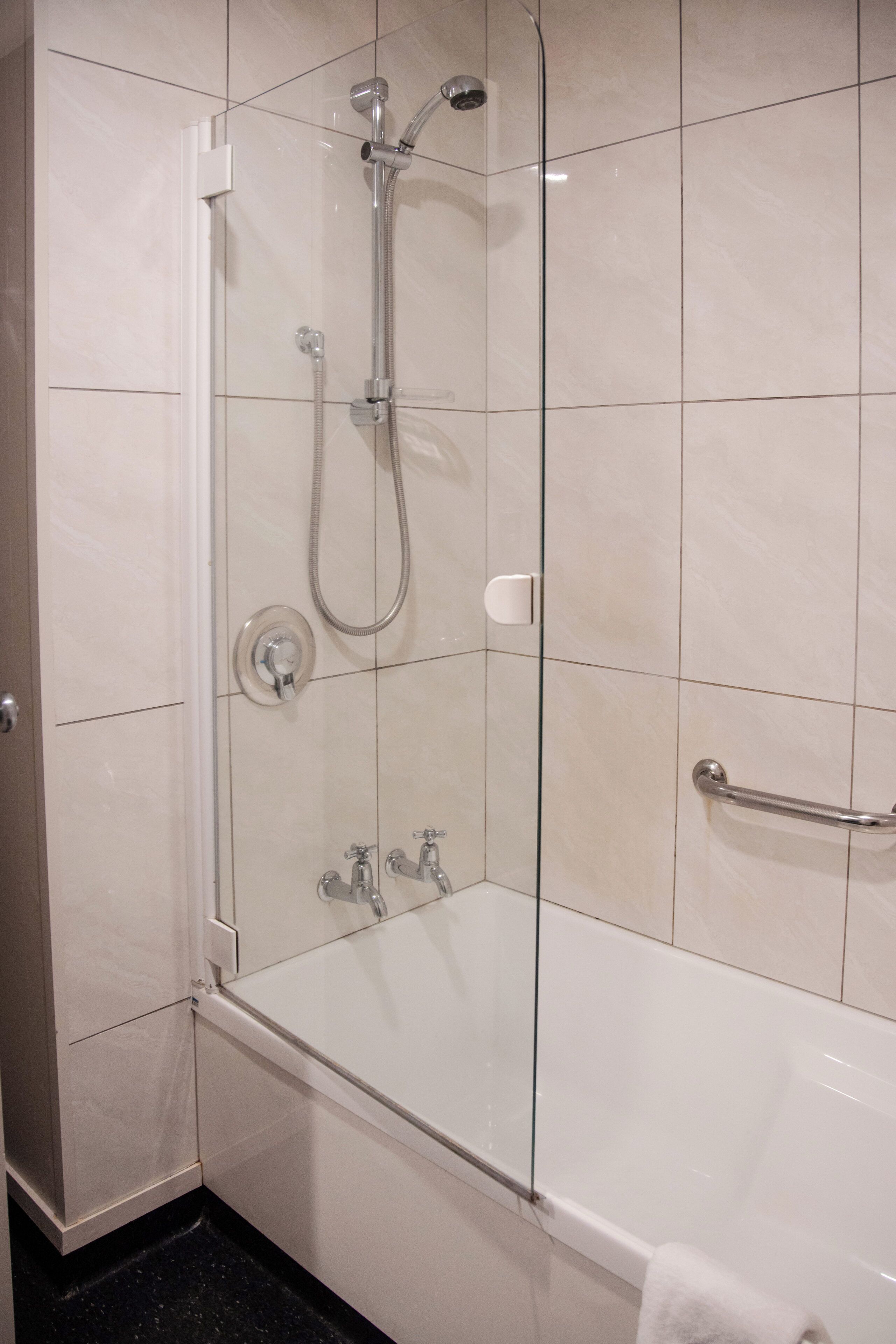 A modern bathroom with a glass-enclosed shower, a white bathtub, and a handrail.