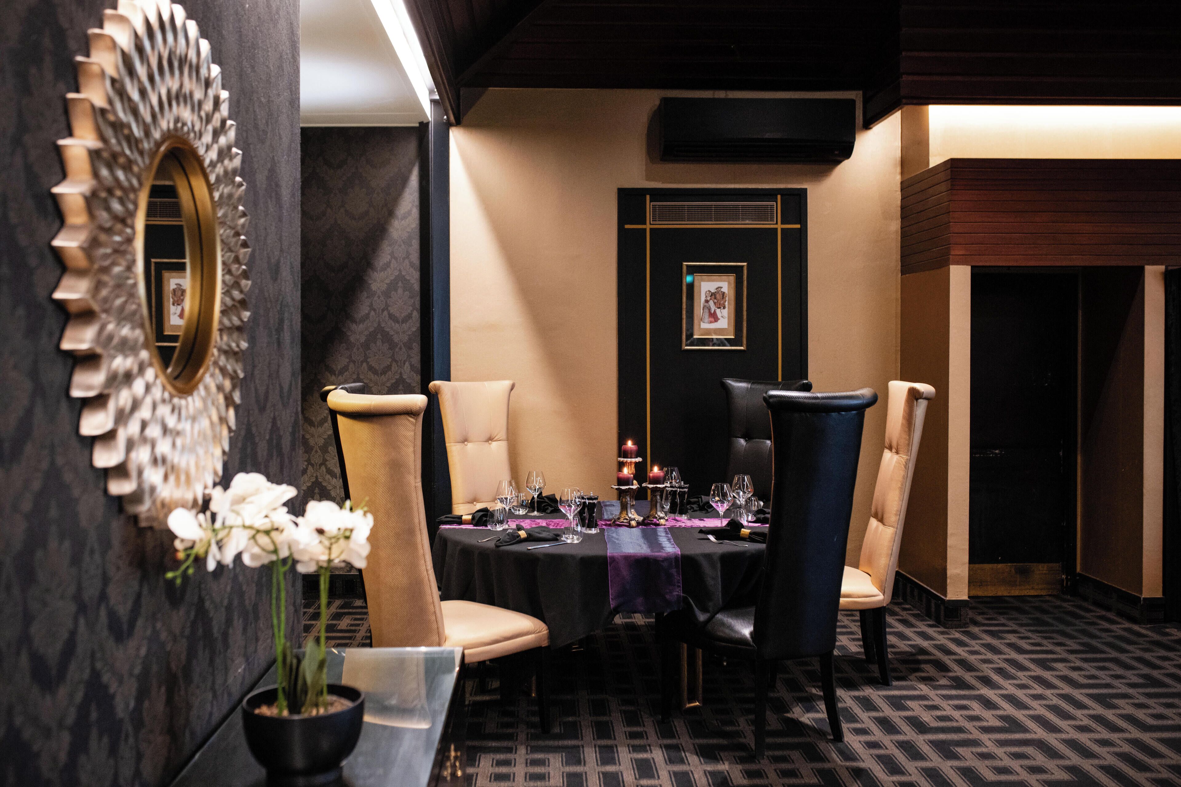 Un comedor con una mesa redonda dispuesta para cuatro personas, rodeada de sillas tapizadas. En la mesa hay un espejo decorativo y un jarrón con flores blancas.