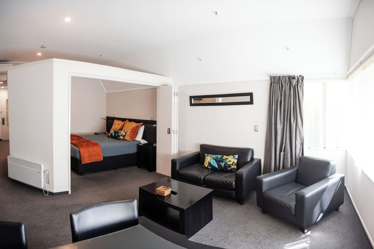 A modern hotel room with a bed, a sofa, a coffee table, and a window with curtains.