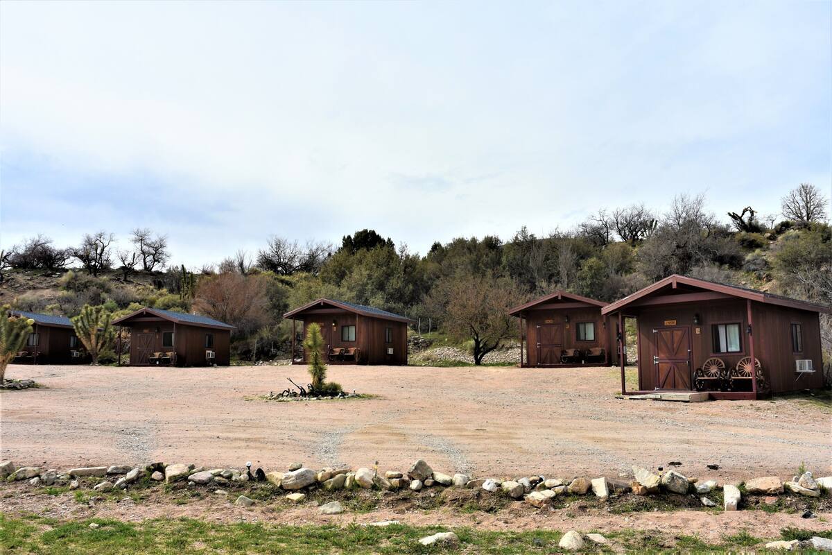 A row of rustic cabins with a gravel driveway and a stone wall in the foreground.