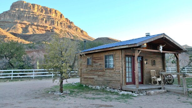 A rustic wooden cabin with a red door, a porch with a rocking chair, and a wagon wheel.