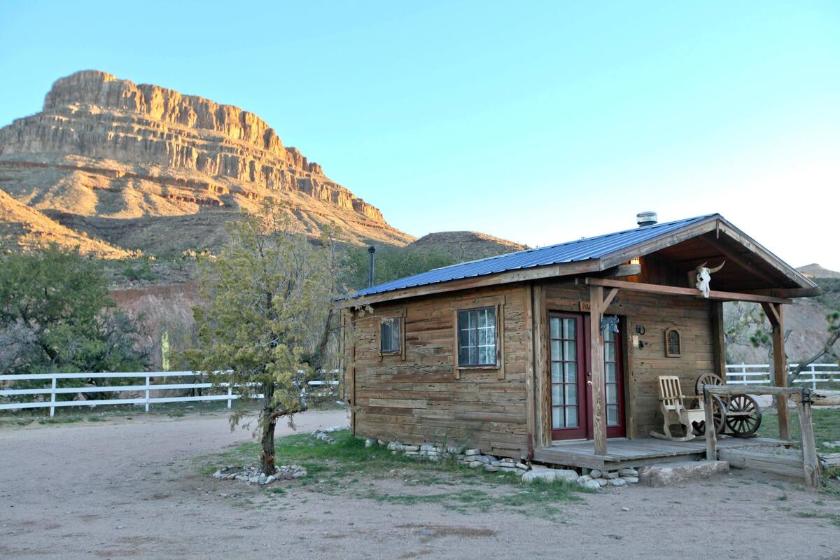 A rustic wooden cabin with a red door, a porch with a rocking chair, and a wagon wheel.