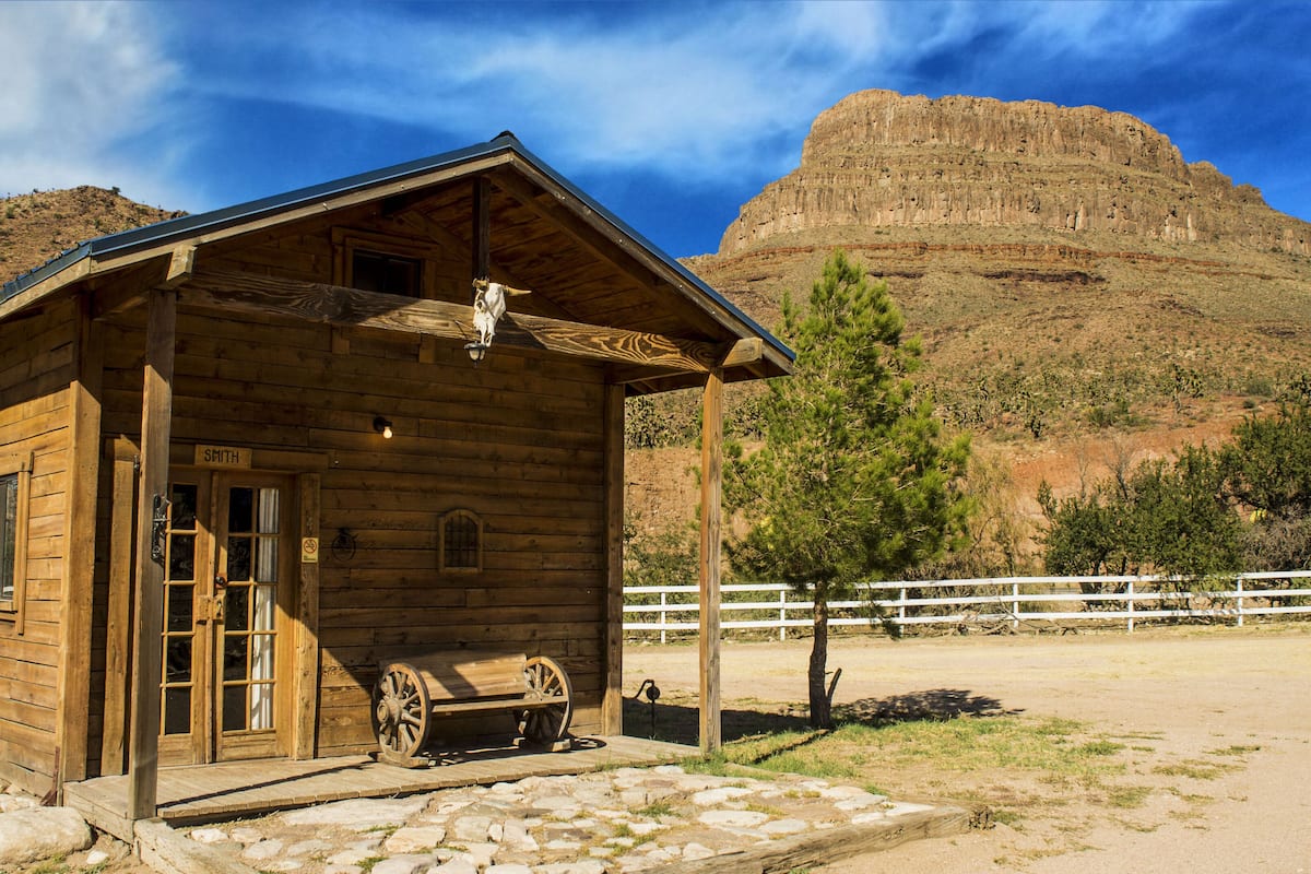 A wooden cabin with a porch, a sign reading "SMITH", and a wagon wheel outside.