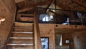 Uma escada de madeira leva a um mezanino com corrimão preto, uma janela com cortinas e um abajur fixado na parede.