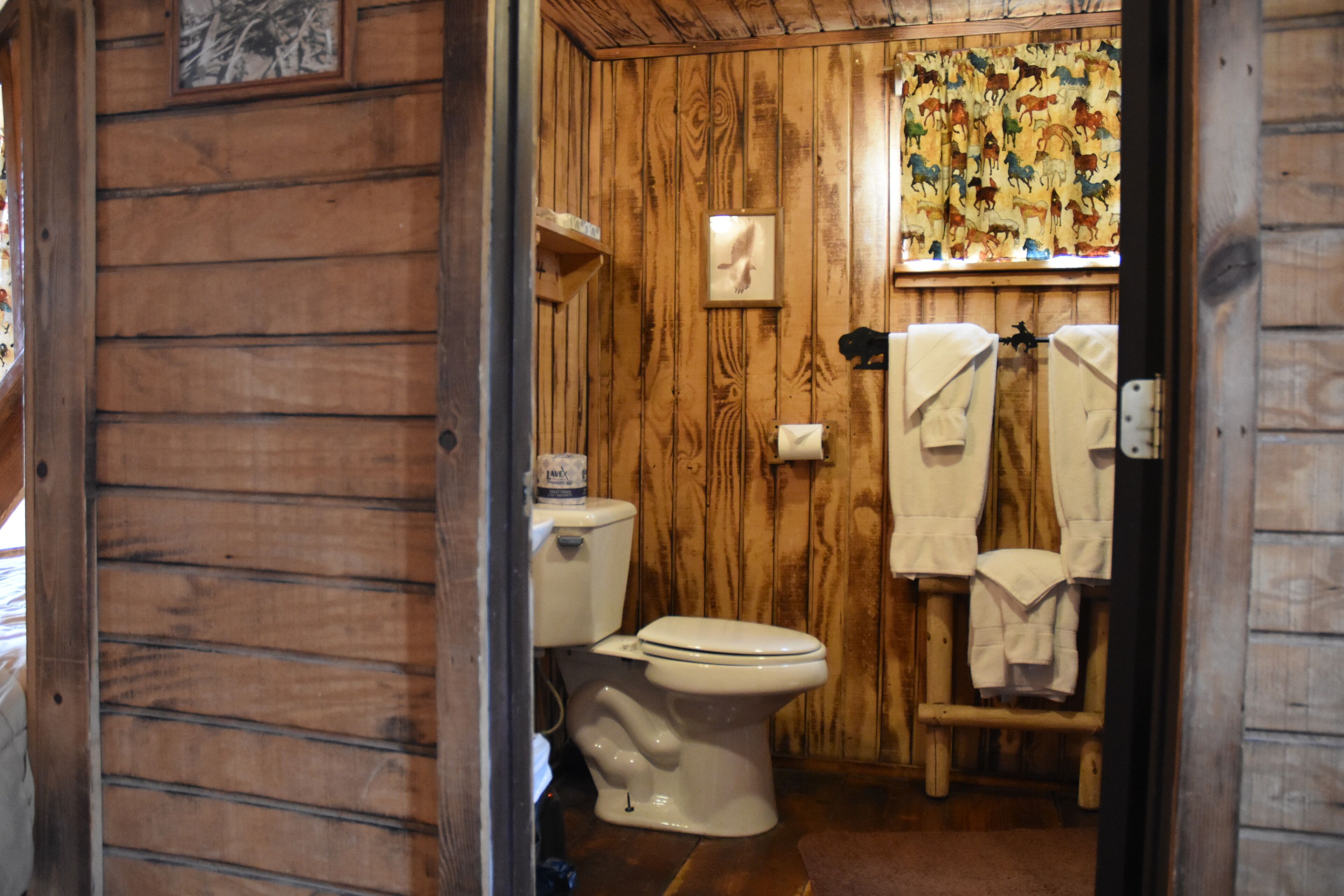 Een houten badkamer met een toilet, een handdoekhouder en een wandplank.