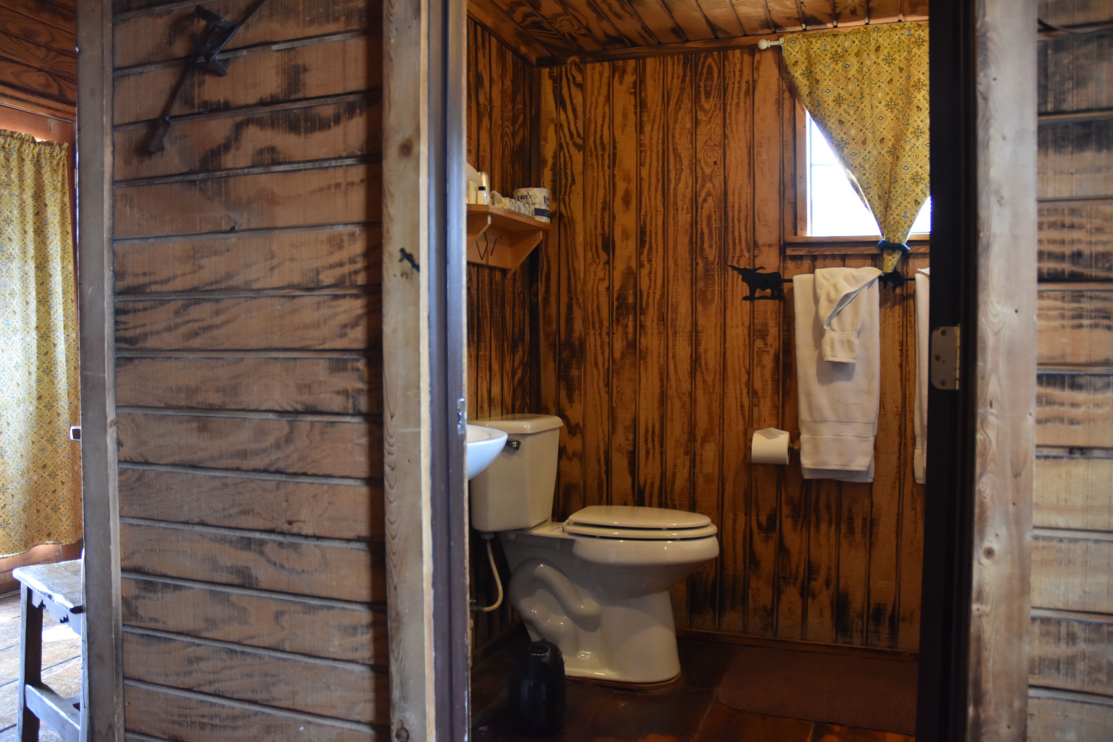 Ein Badezimmer einer Holzhütte mit Toilette, Waschbecken und einem Fenster mit Vorhang.