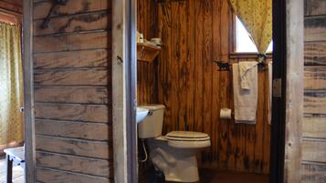 Ein Badezimmer einer Holzhütte mit Toilette, Waschbecken und einem Fenster mit Vorhang.