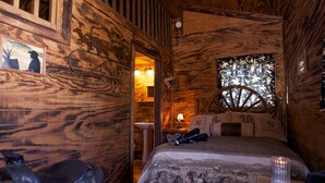 Um quarto rústico de madeira com uma cama, uma sela e um abajur.