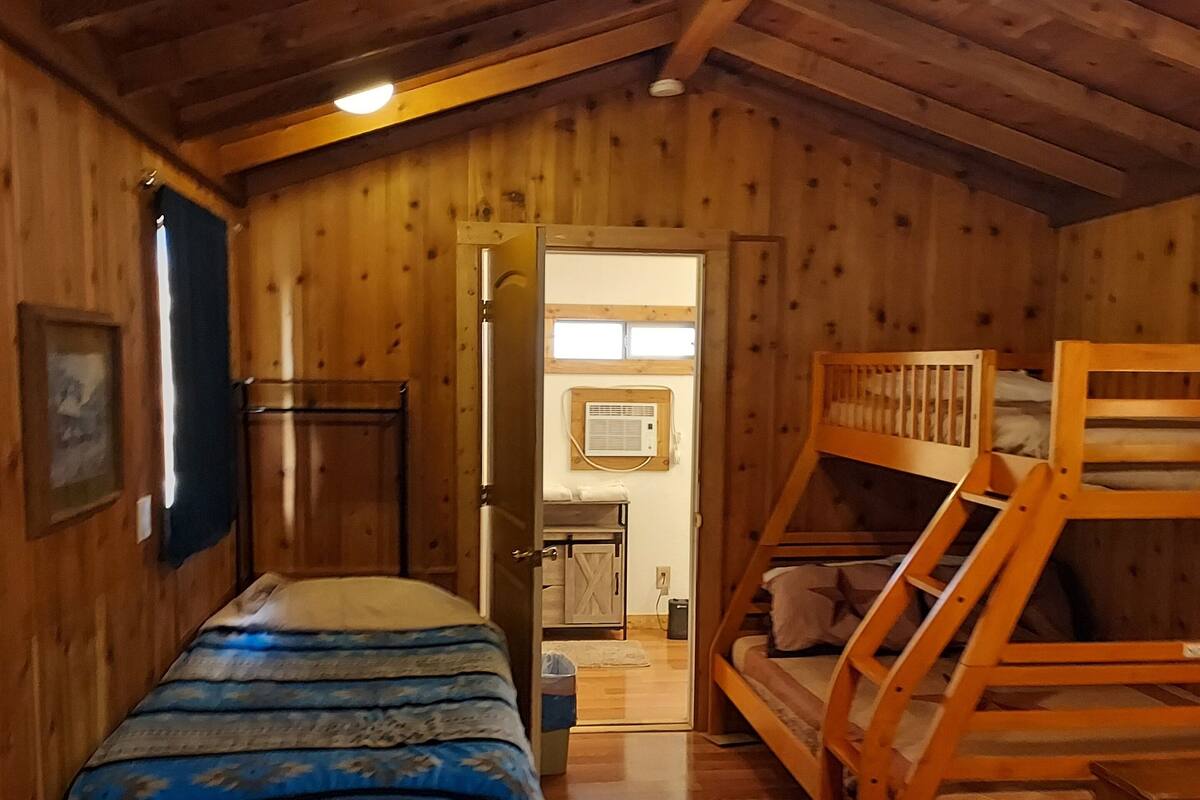 A wooden cabin room with a bunk bed, a single bed, and a small table.