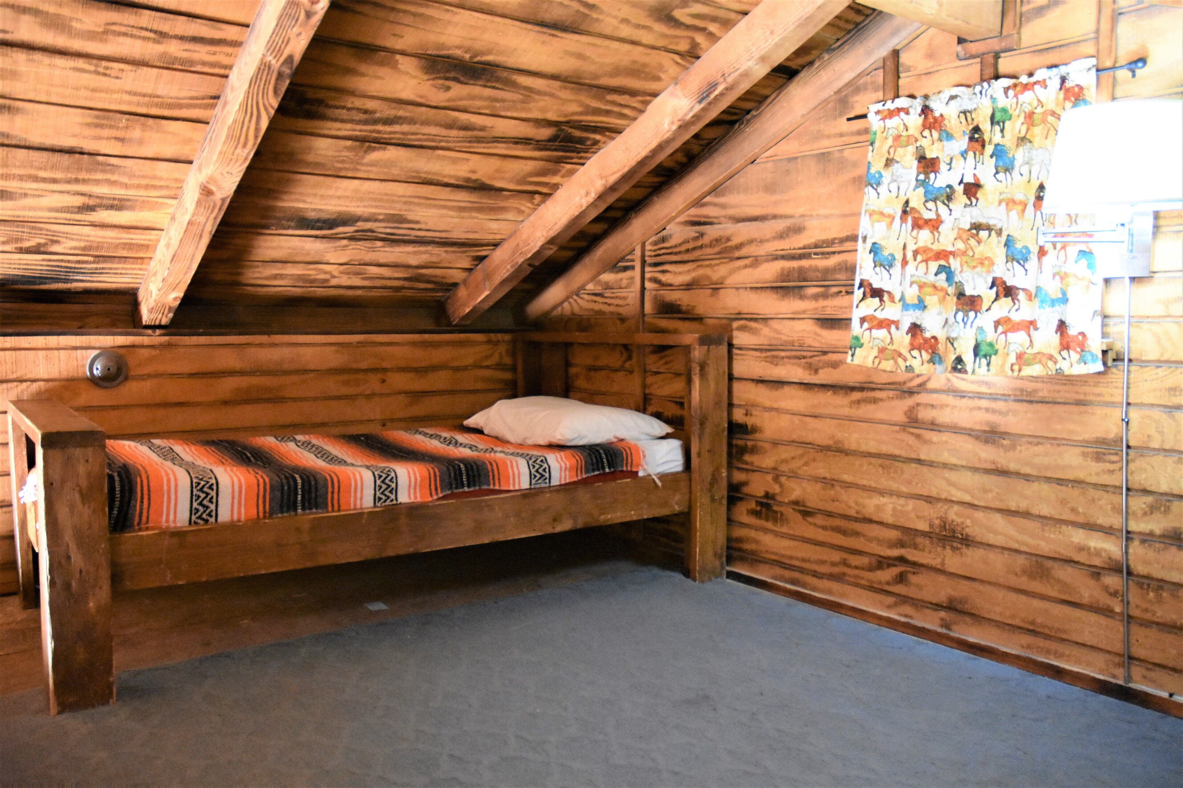 Een houten kamer met een bed, een houten plafond en een wand met een decoratief gordijn.
