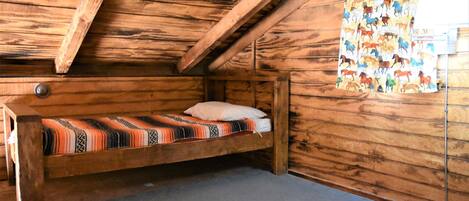 Een houten kamer met een bed, een houten plafond en een wand met een decoratief gordijn.