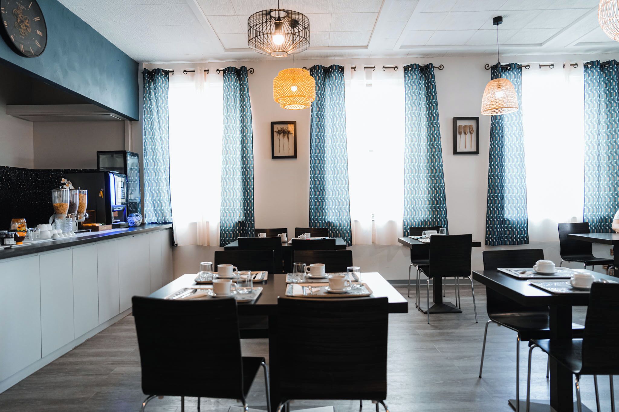 A modern dining area with black chairs and tables, blue patterned curtains, and pendant lights.