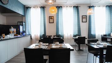 A modern dining area with black chairs and tables, blue patterned curtains, and pendant lights.
