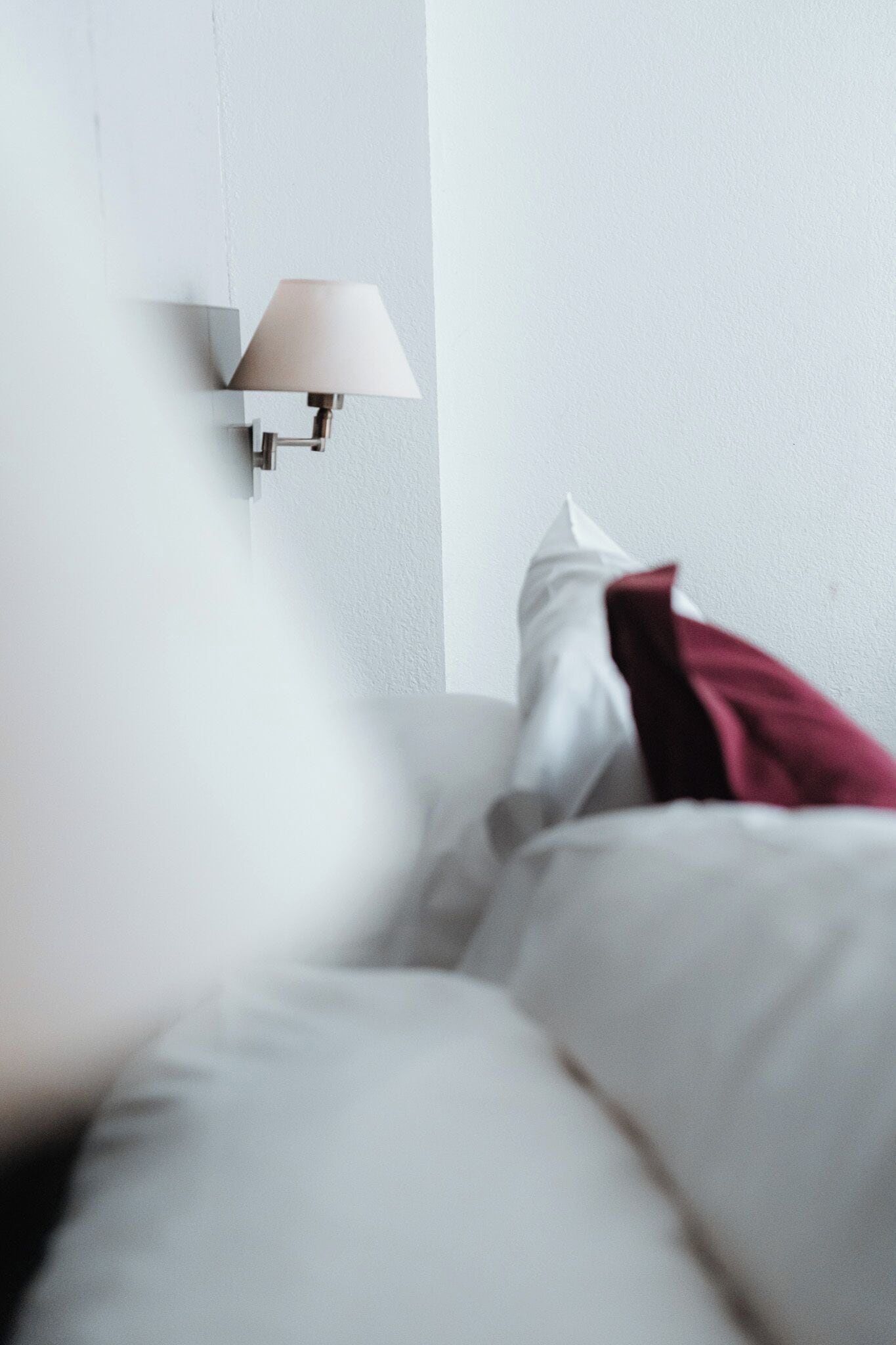 A bedroom with a bed, pillows, and a wall-mounted lamp.