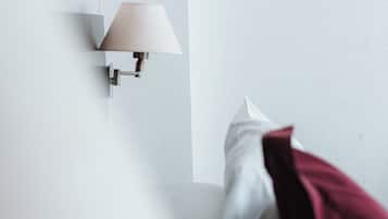 A bedroom with a bed, pillows, and a wall-mounted lamp.