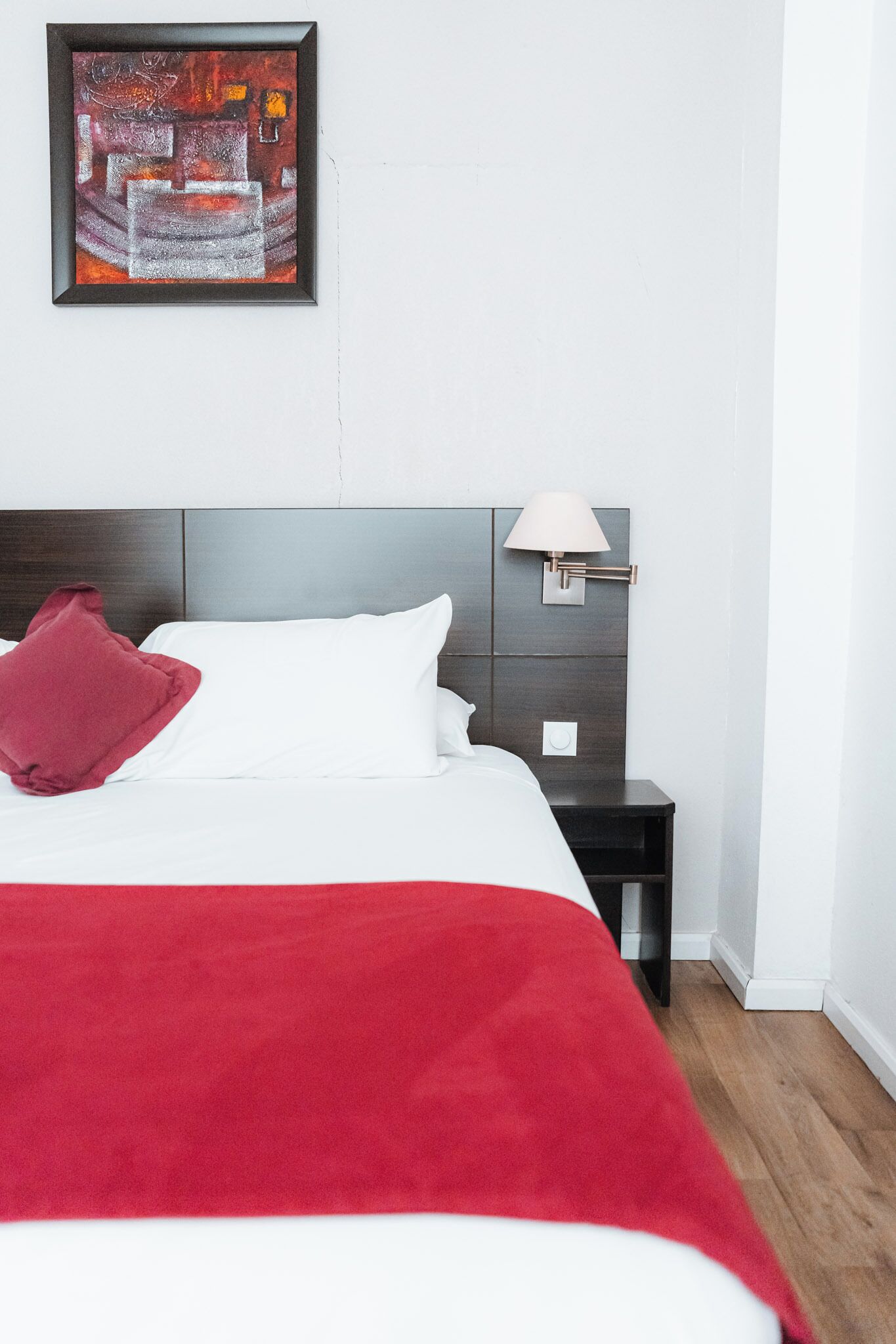 Een hotelkamer met een bed, nachtkastje, lamp en een schilderij aan de muur.