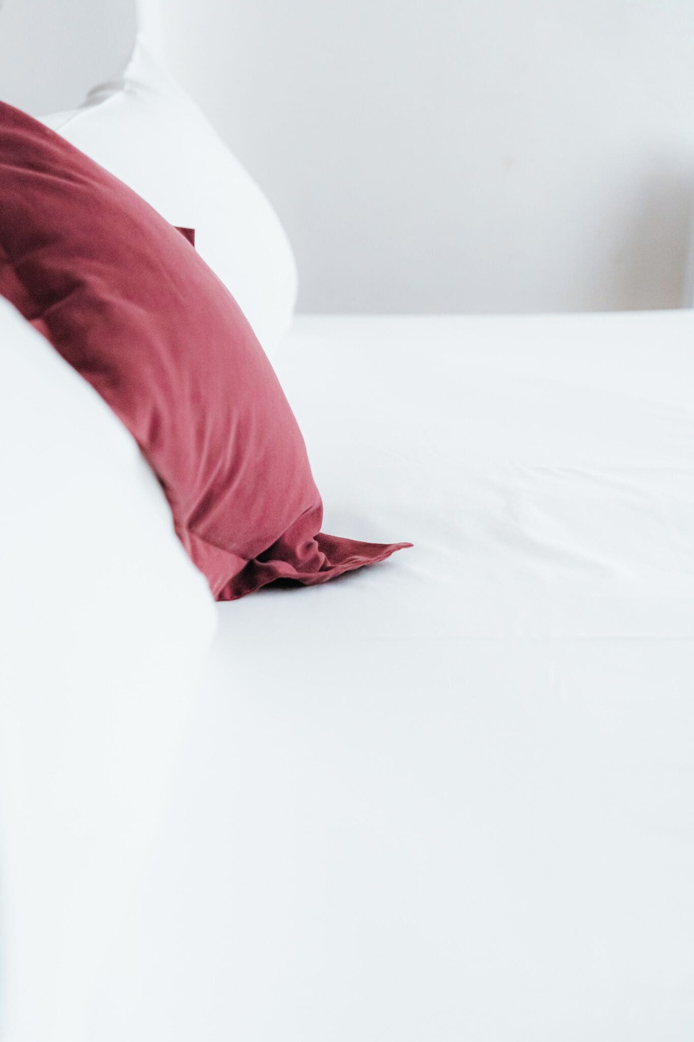 A bed with a white sheet and a single red pillow.