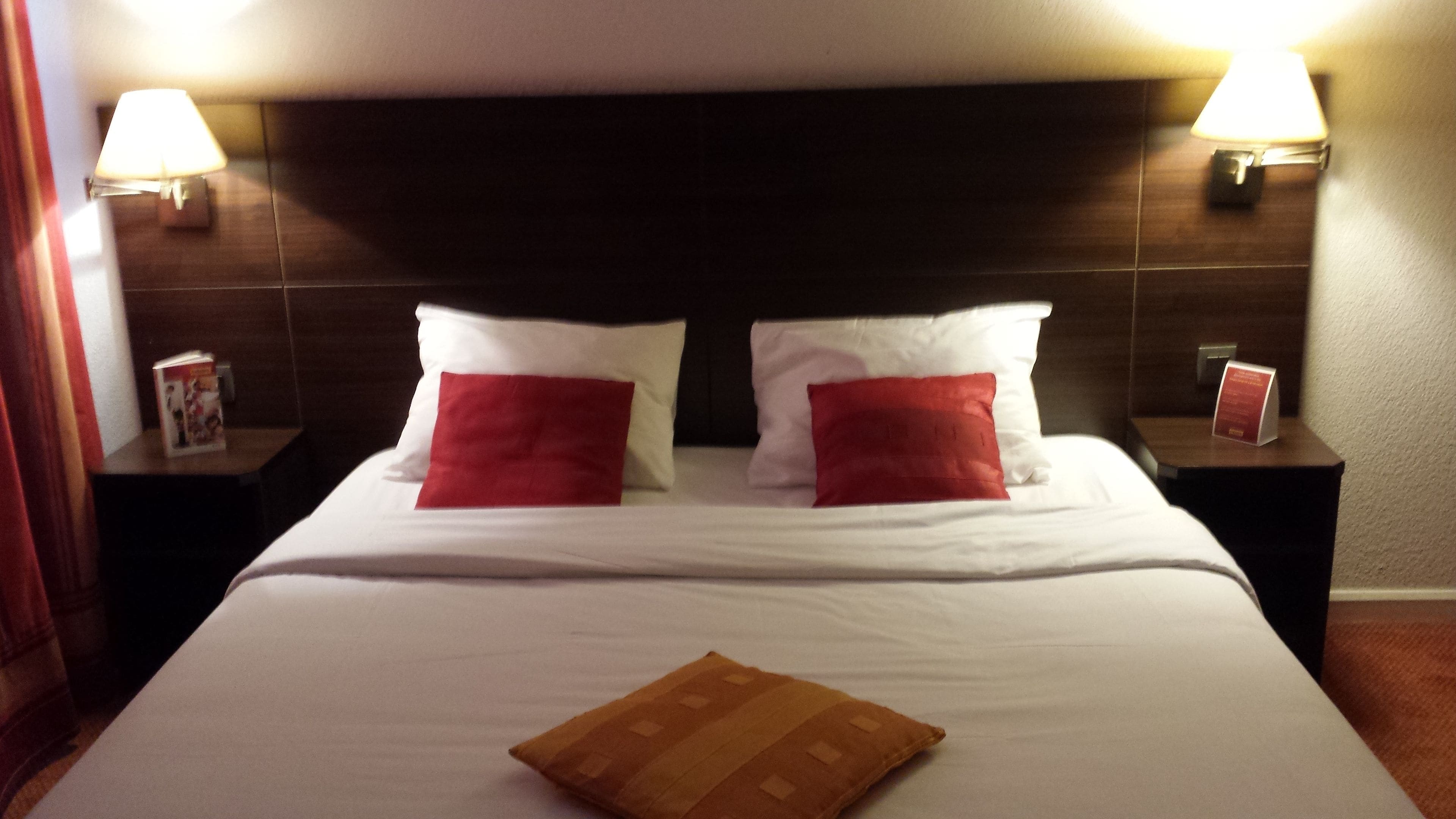 A hotel room with a large bed, two bedside tables, and two wall-mounted lamps.