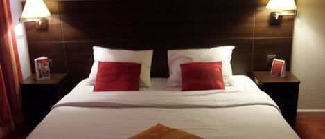 Una habitación de hotel con una cama grande, dos mesitas de noche y dos lámparas de pared.