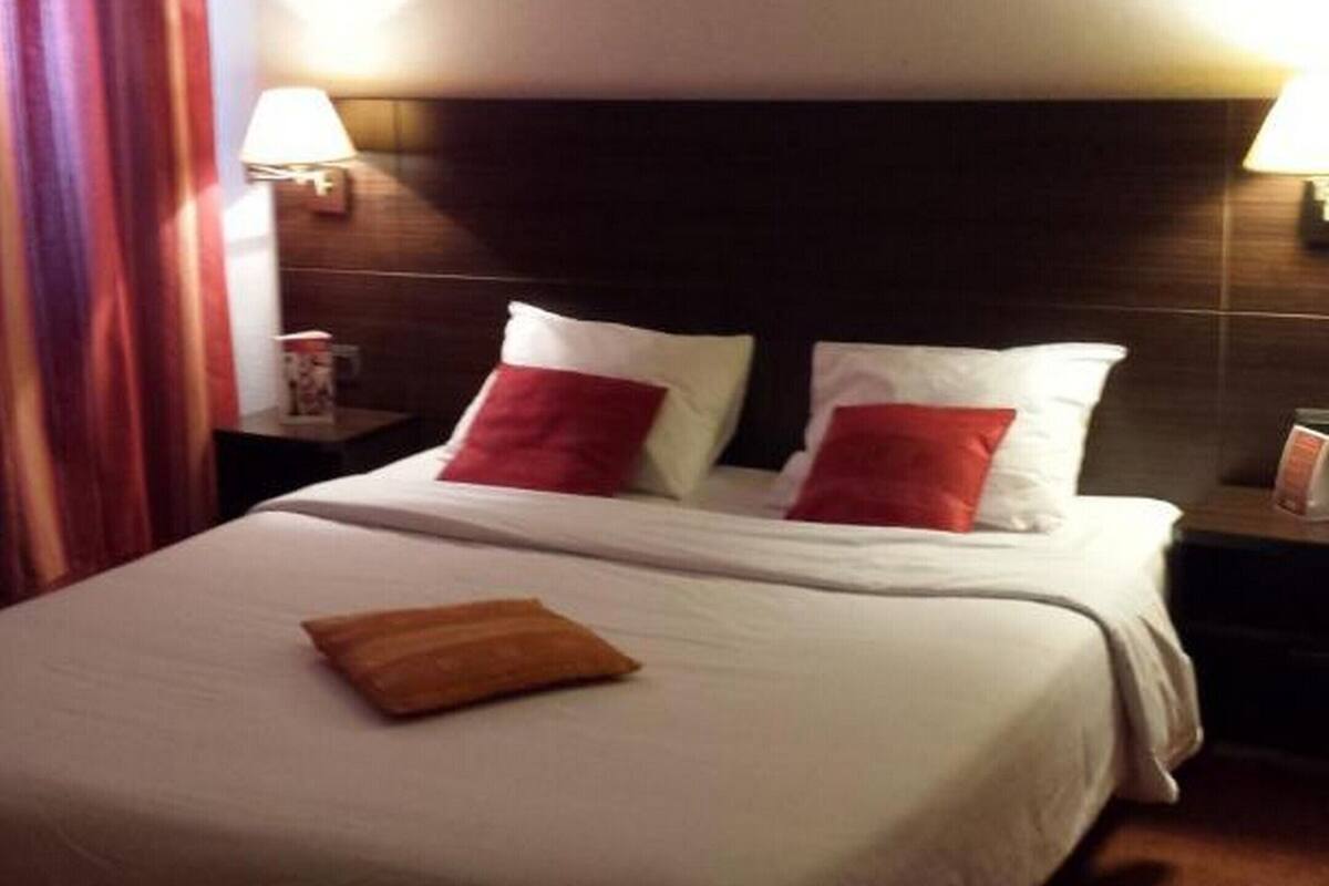 A hotel room with a bed, pillows, a nightstand, and a lamp.