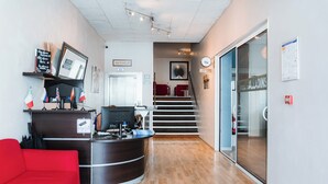 A reception area with a desk, a red sofa, a staircase, and a glass door leading to another room. - urban by balladins Perpignan (Perpignan)