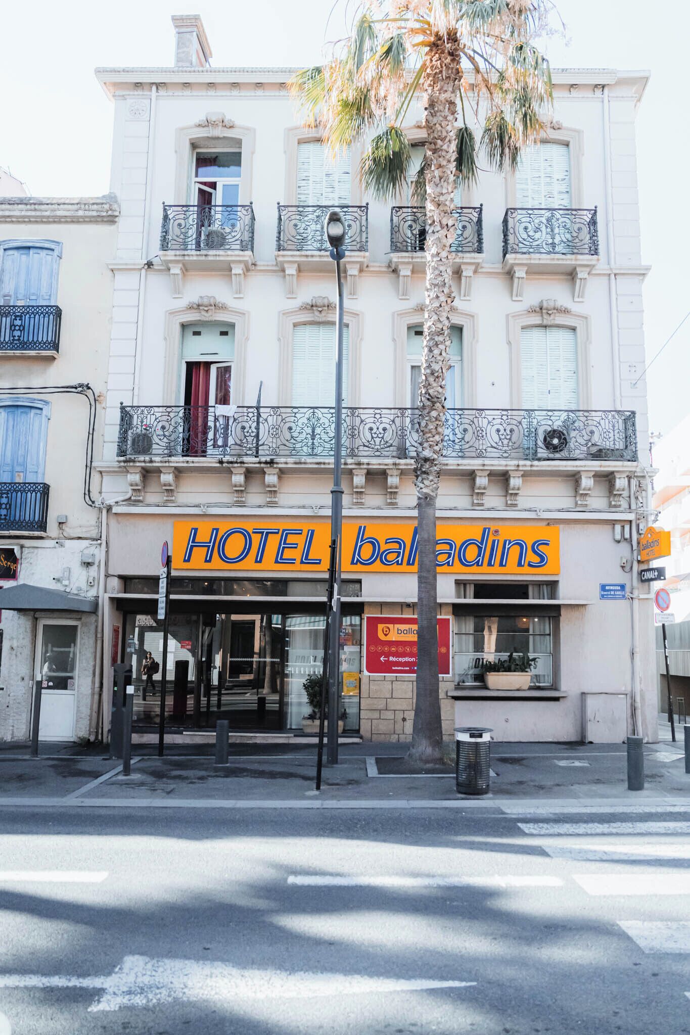 A hotel named "HOTEL baladins" with a classic facade, a palm tree in front, and a street view.