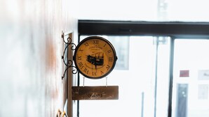 A hallway with a wall-mounted clock, a door with a sign, and a glimpse of a building outside. - urban by balladins Perpignan (Perpignan)
