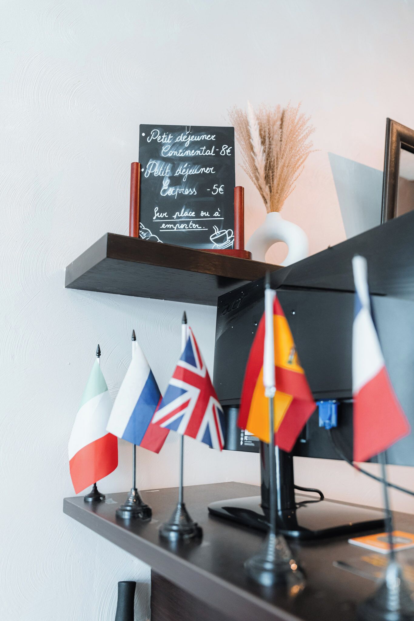 A shelf with flags, a chalkboard menu, and a vase with dried plants.