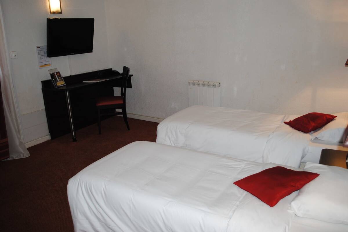 A hotel room with two beds, a desk, and a TV.