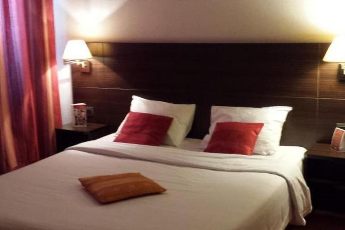 A hotel room with a bed, pillows, a nightstand, and a lamp.