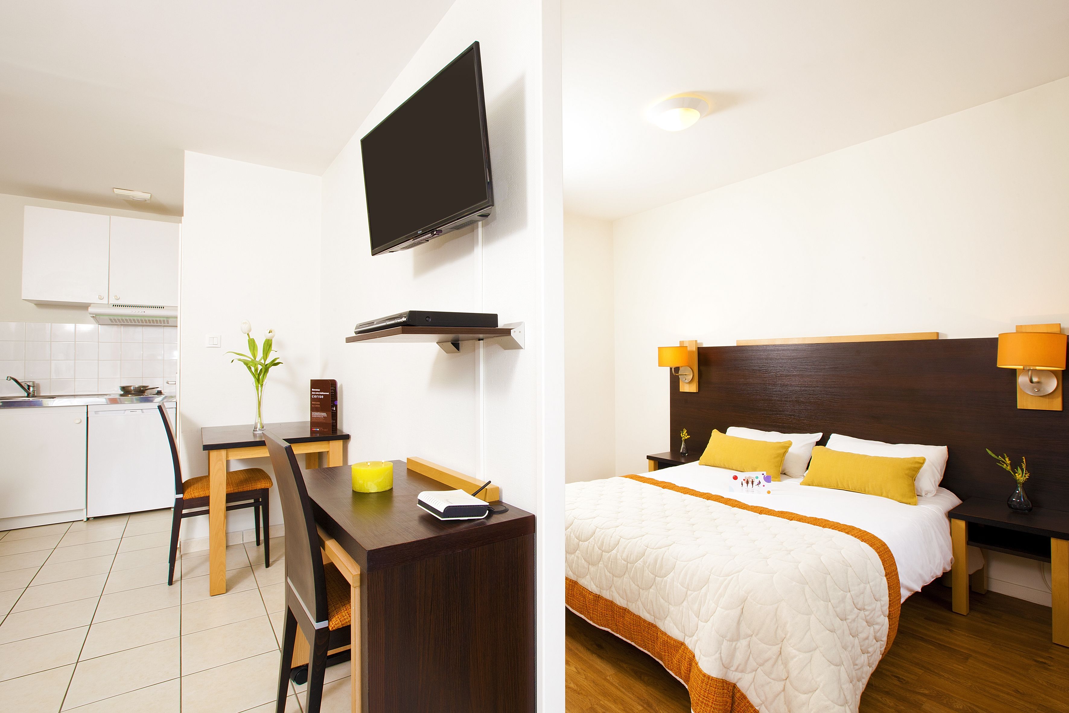 A hotel room with a bed, bedside table, lamp, and a TV mounted on the wall.