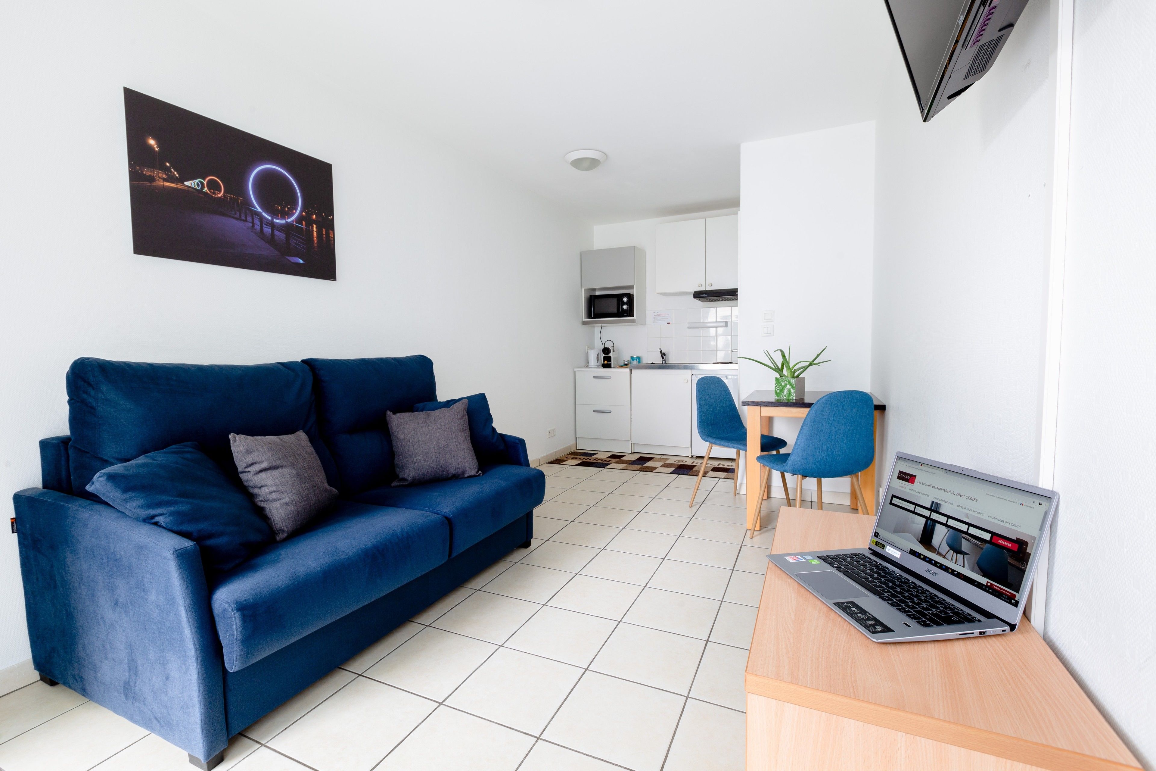 A modern living room with a blue sofa, a laptop on a desk, and a kitchen in the background.