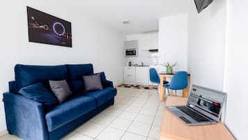 A modern living room with a blue sofa, a laptop on a desk, and a kitchen in the background.