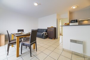 Un salon moderne comprenant un coin repas, un canapé gris, un petit meuble et un coin cuisine équipé d’un four à micro-ondes.