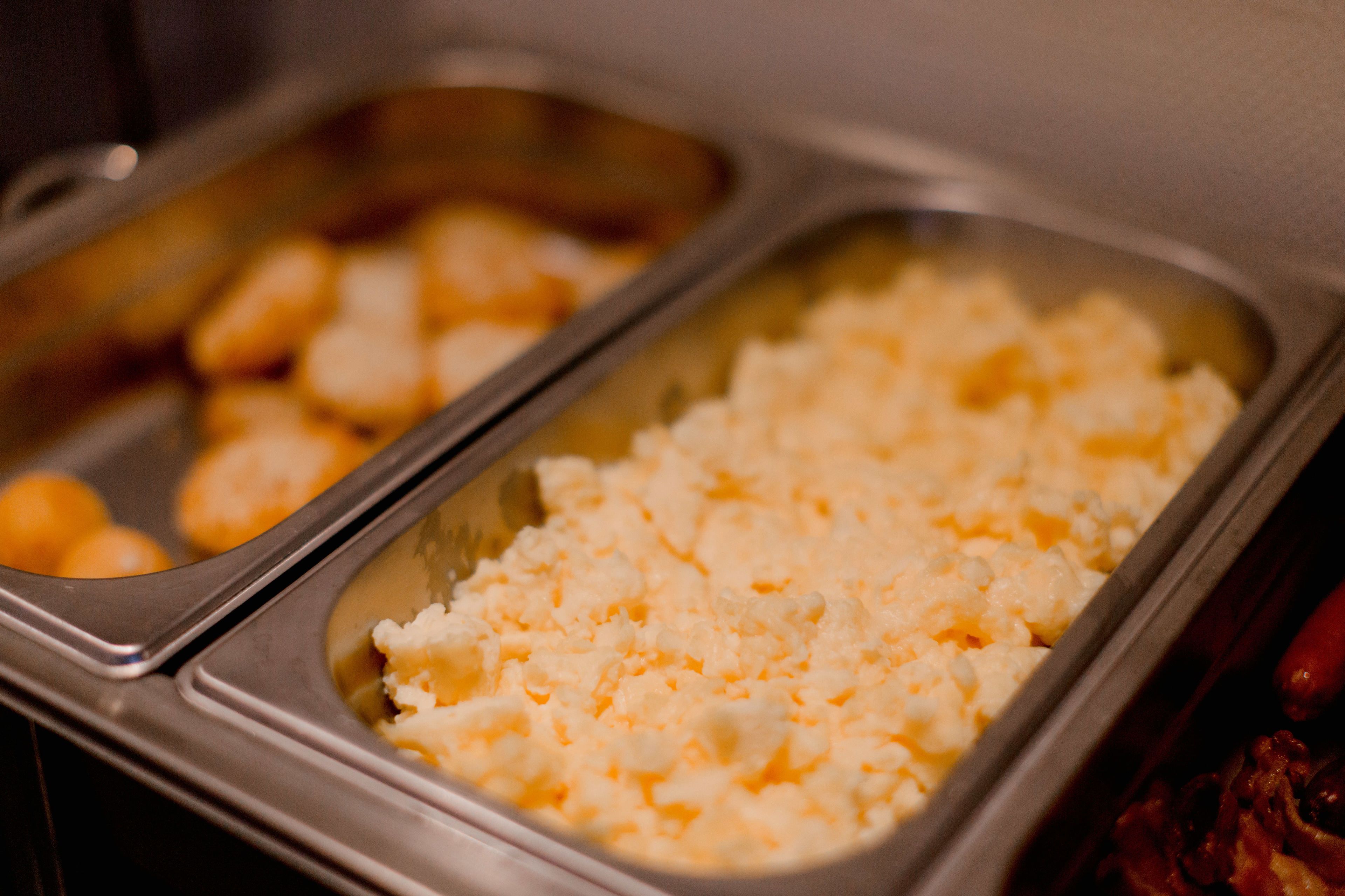 Un buffet avec deux plateaux de nourriture : l’un contient ce qui ressemble à des œufs brouillés et l’autre, un plat crémeux, peut-être un gratin ou une salade de macaronis.