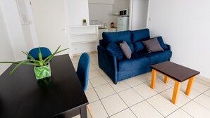 Una sala moderna con un sofá azul, una mesita de madera y una mesa baja negra. Hay una planta en maceta sobre una mesa negra.