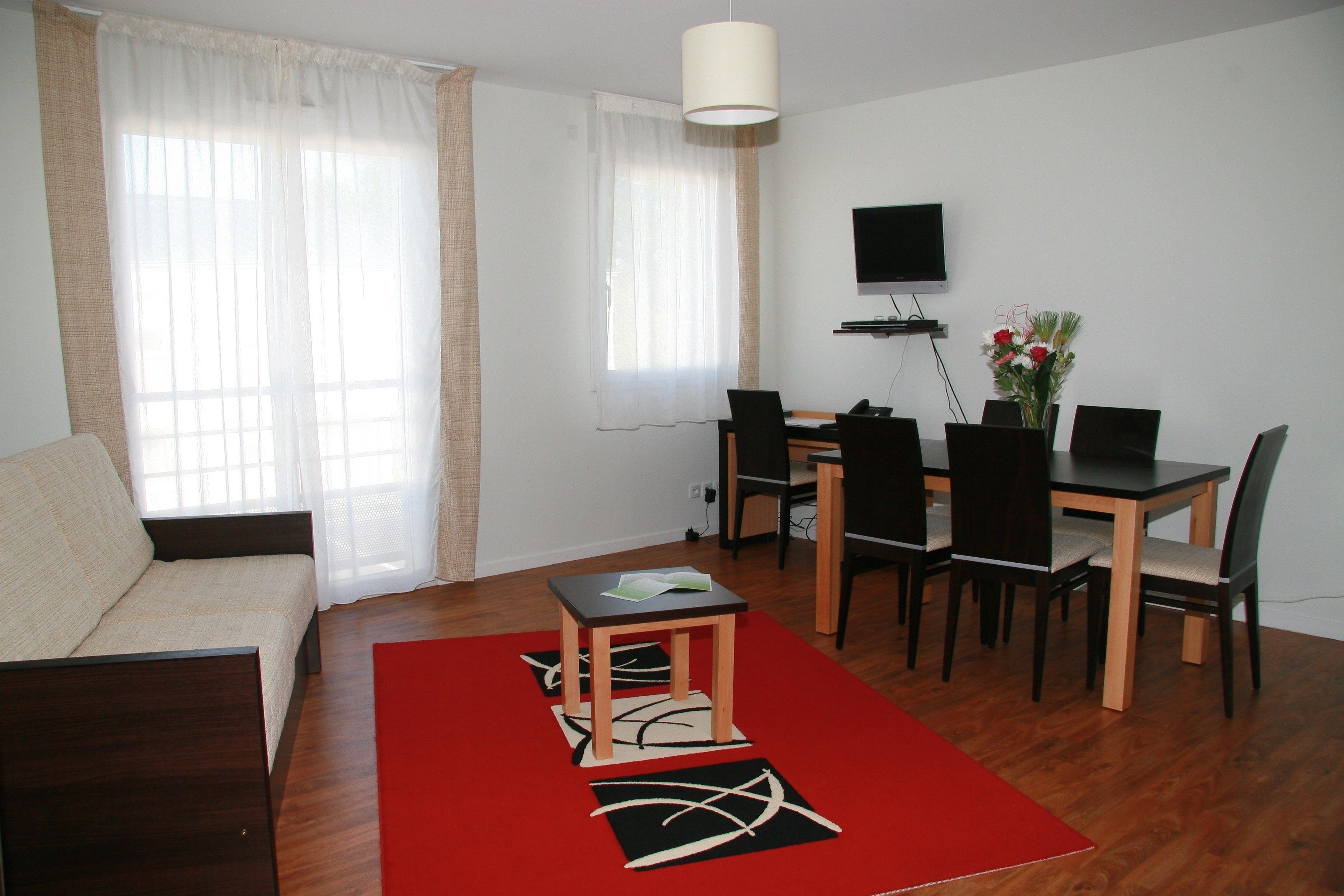 Uma sala de estar moderna com sofá, mesa de jantar, cadeiras, TV e um tapete vermelho.