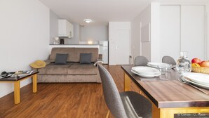 Un salón moderno con sofá, una mesa de comedor con platos y vasos, y una cocina al fondo.