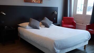 Une chambre d’hôtel avec un grand lit, une tête de lit, deux lampes de chevet, une chaise rouge et une fenêtre avec des rideaux.