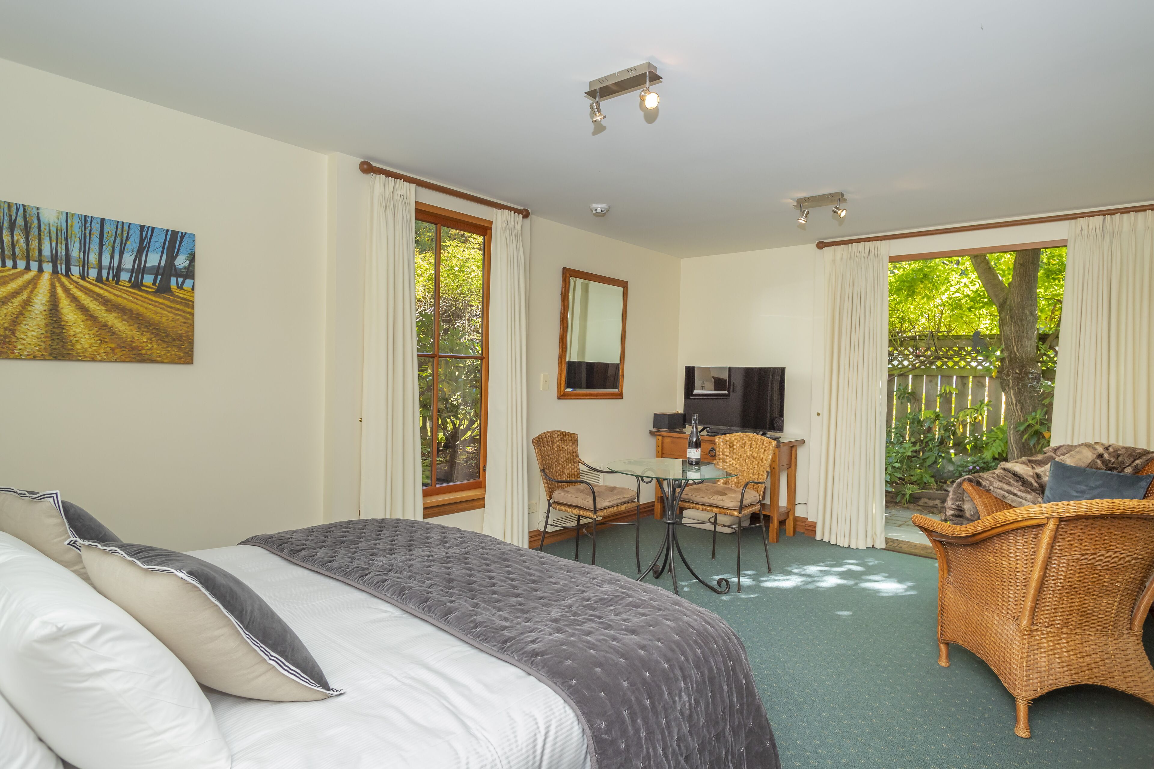 Habitación de hotel con cama, zona de comedor con sillas, televisor y vista a zonas verdes.