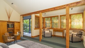 A spacious room with a large bed, two armchairs, a small table, and a television. - Arrowtown House Boutique Accommodation (Arrowtown)