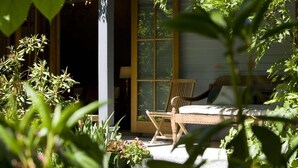 A sunlit porch with a wooden chair and a table, surrounded by lush greenery. - Arrowtown House Boutique Accommodation (Arrowtown)