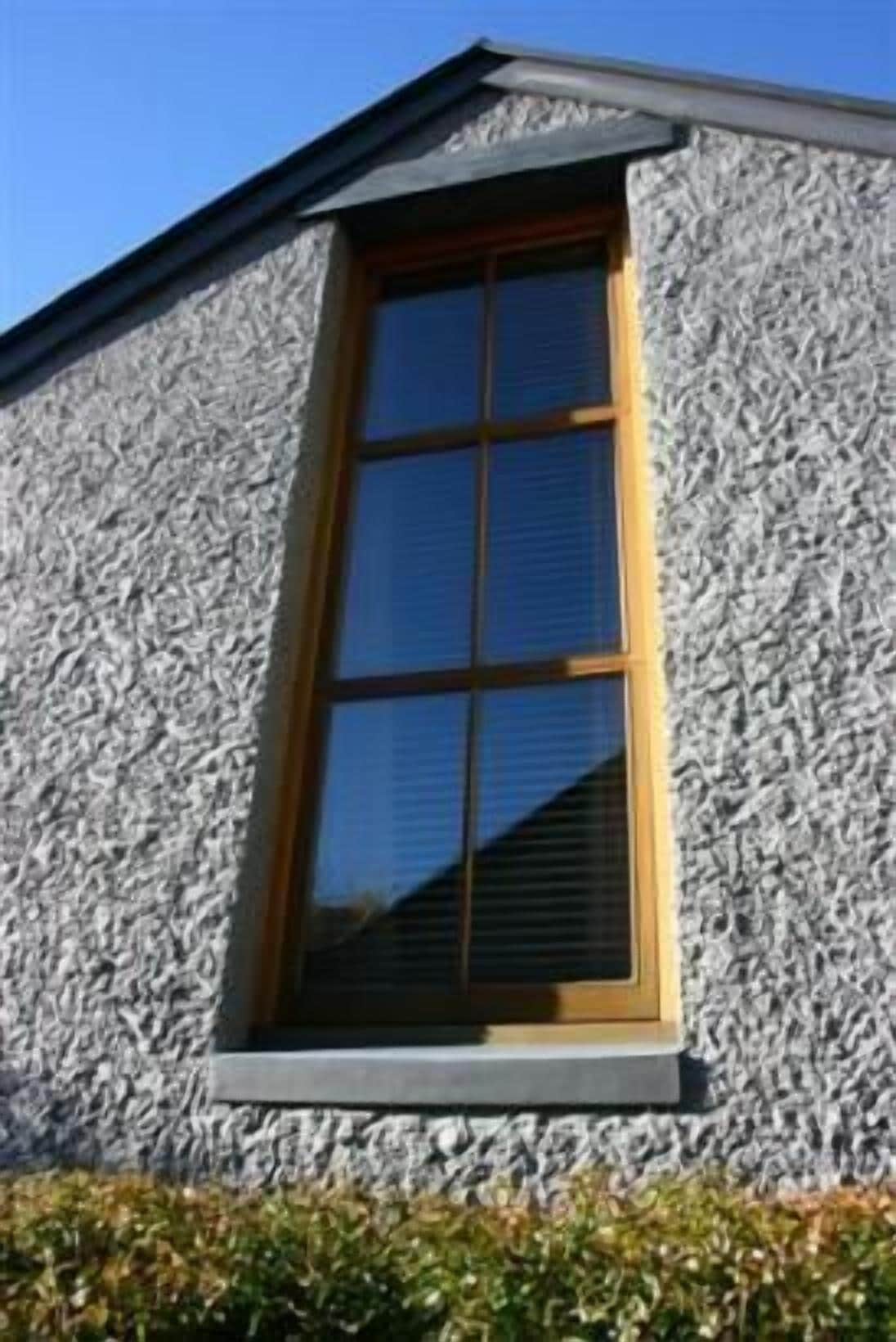 Un bâtiment doté d’une façade en pierre à texture et d’une grande fenêtre à cadre en bois.