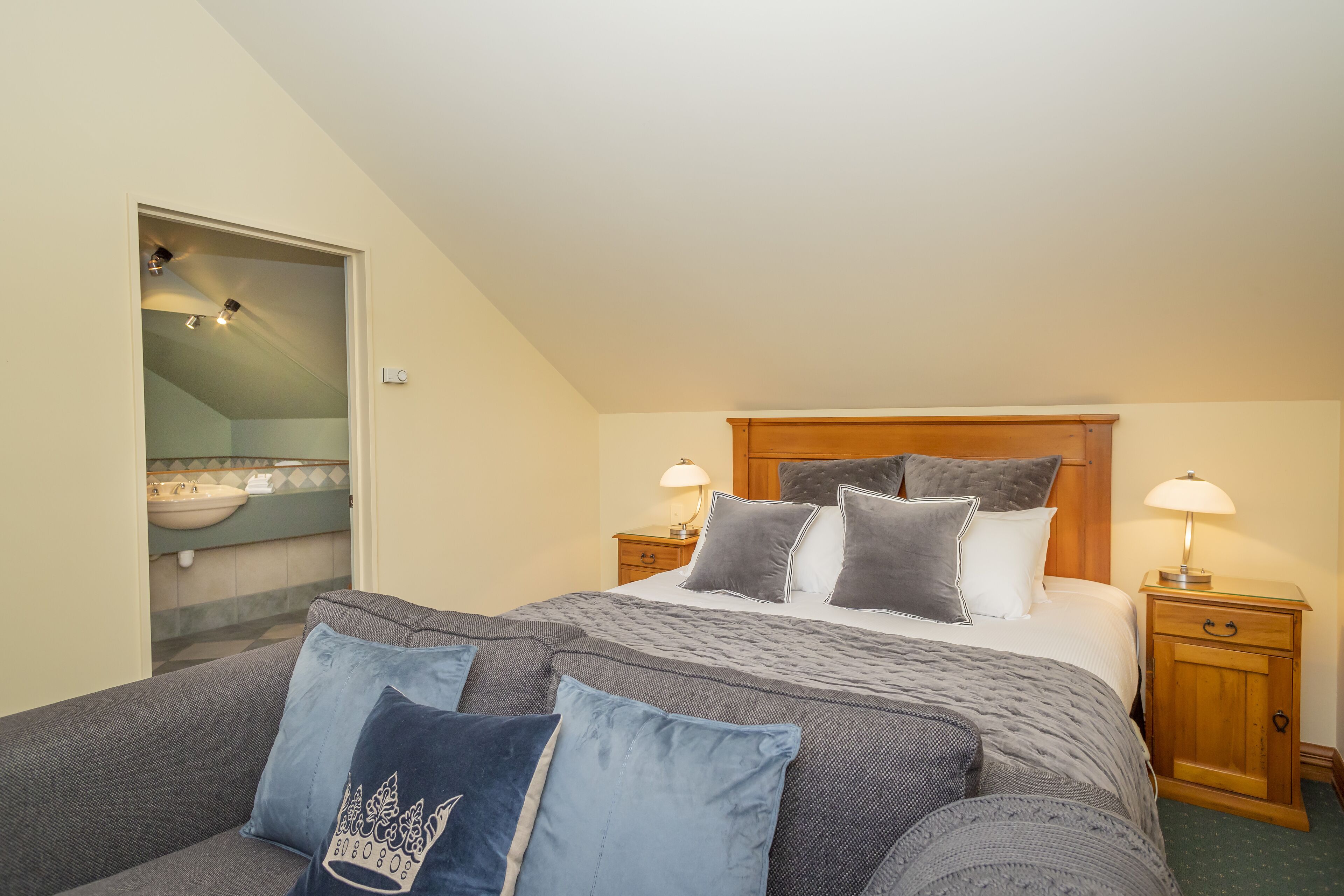 A bedroom with a bed, two bedside tables, a nightstand, a sofa, and a bathroom visible through an open door.