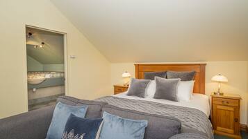 A bedroom with a bed, two bedside tables, a nightstand, a sofa, and a bathroom visible through an open door.