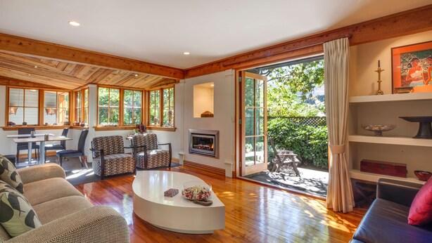 A spacious living room with a fireplace, a dining area, and a large sliding glass door leading to a patio. - Arrowtown House Boutique Accommodation (Arrowtown)