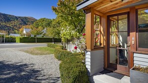 A wooden building with a glass door, surrounded by a gravel driveway and a well-maintained hedge. - Arrowtown House Boutique Accommodation (Arrowtown)